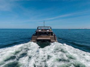A Sunreef Yachts catamaran named Aganippe cruises on the open sea, leaving a foamy wake behind under a clear blue sky.