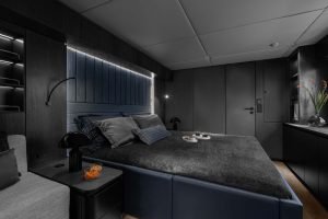 Interior view of a luxurious bedroom on a Sunreef Yachts vessel, featuring a dark, modern design with a large bed, seating area, and ambient lighting.