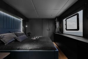 A luxurious bedroom inside a Sunreef Yachts vessel with a large bed, elegant decor, and a sea view through a window.